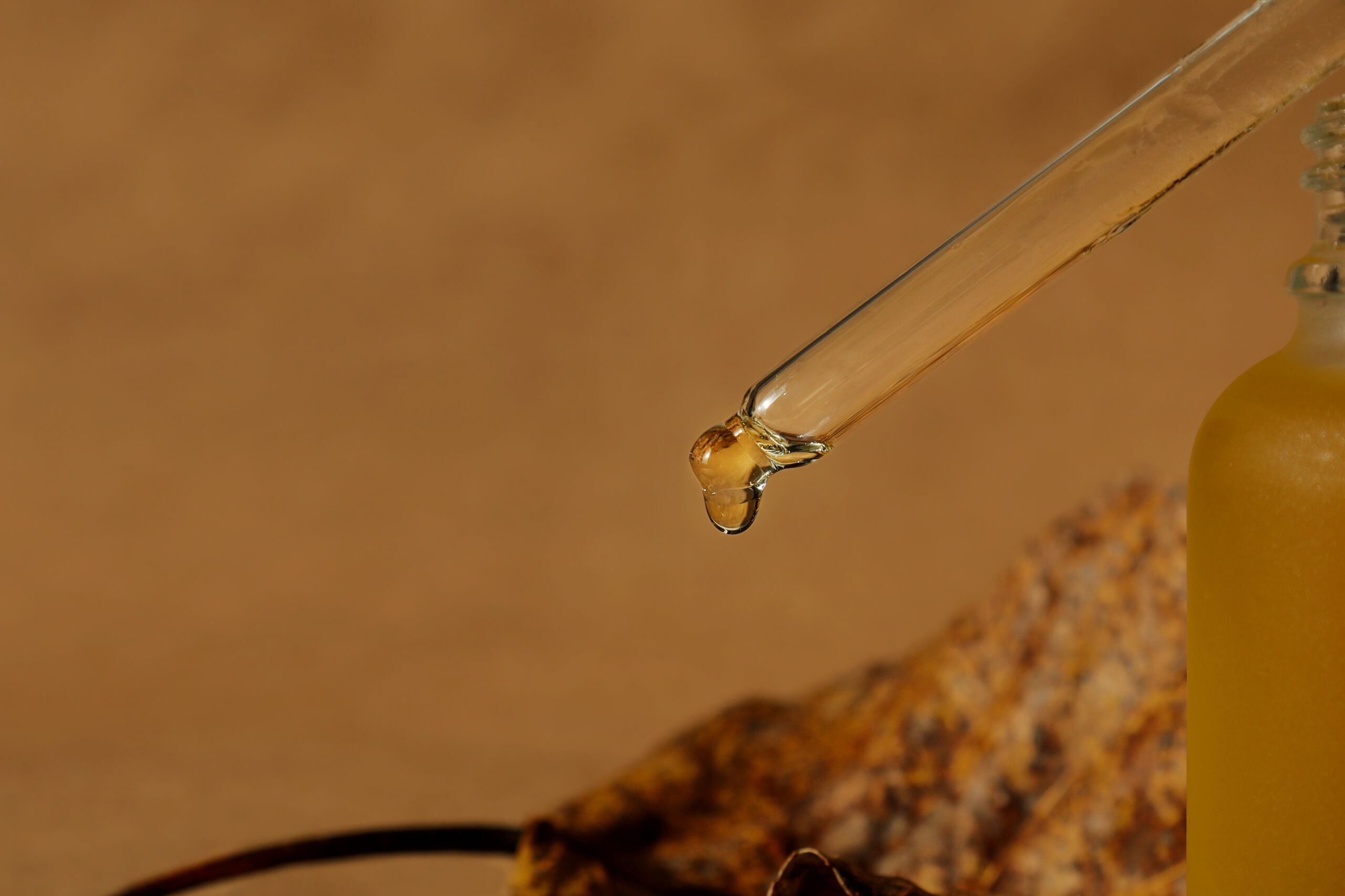 Glass pipette with drop of aroma oil. Dropper with lotion, essence, serum, emulsion. Horizontal monochrome banner, poster, copy space, brown craft background. Natural organic cosmetic. Dark moody